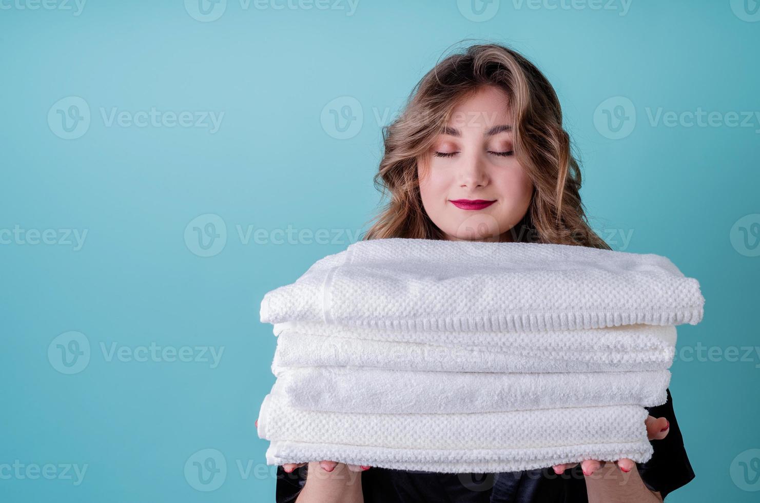 dona de casa feliz segurando uma pilha de toalhas brancas limpas isoladas em um fundo azul foto