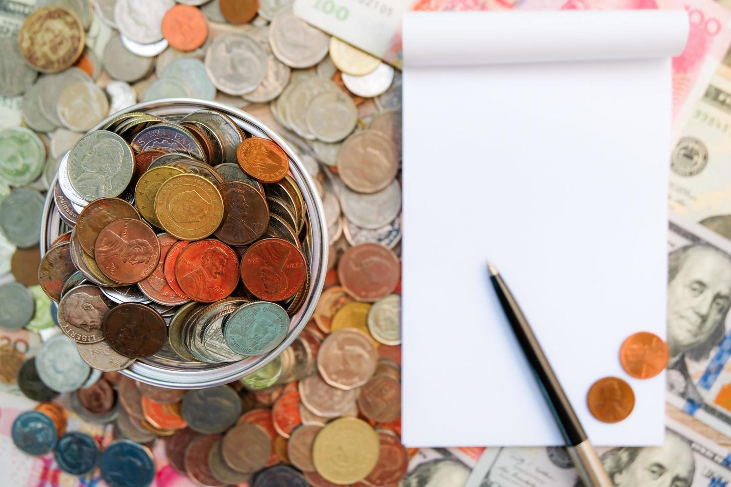 caderno em branco vazio com pilha de moedas e notas de várias cores. receita de gestão e conceito de economia. foto