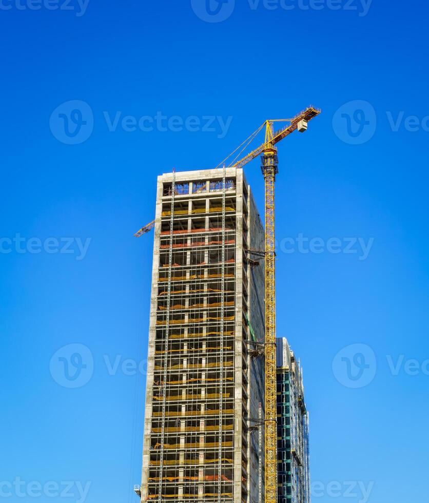 uma guindaste construção uma moderno arranha-céu contra uma azul céu. construção local. foto