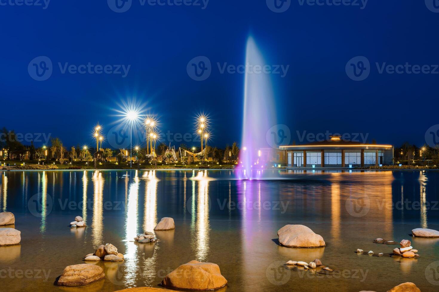 borrado fonte água fluxos dentro a artificial lago dentro uma noite parque com lanternas e decorações. foto