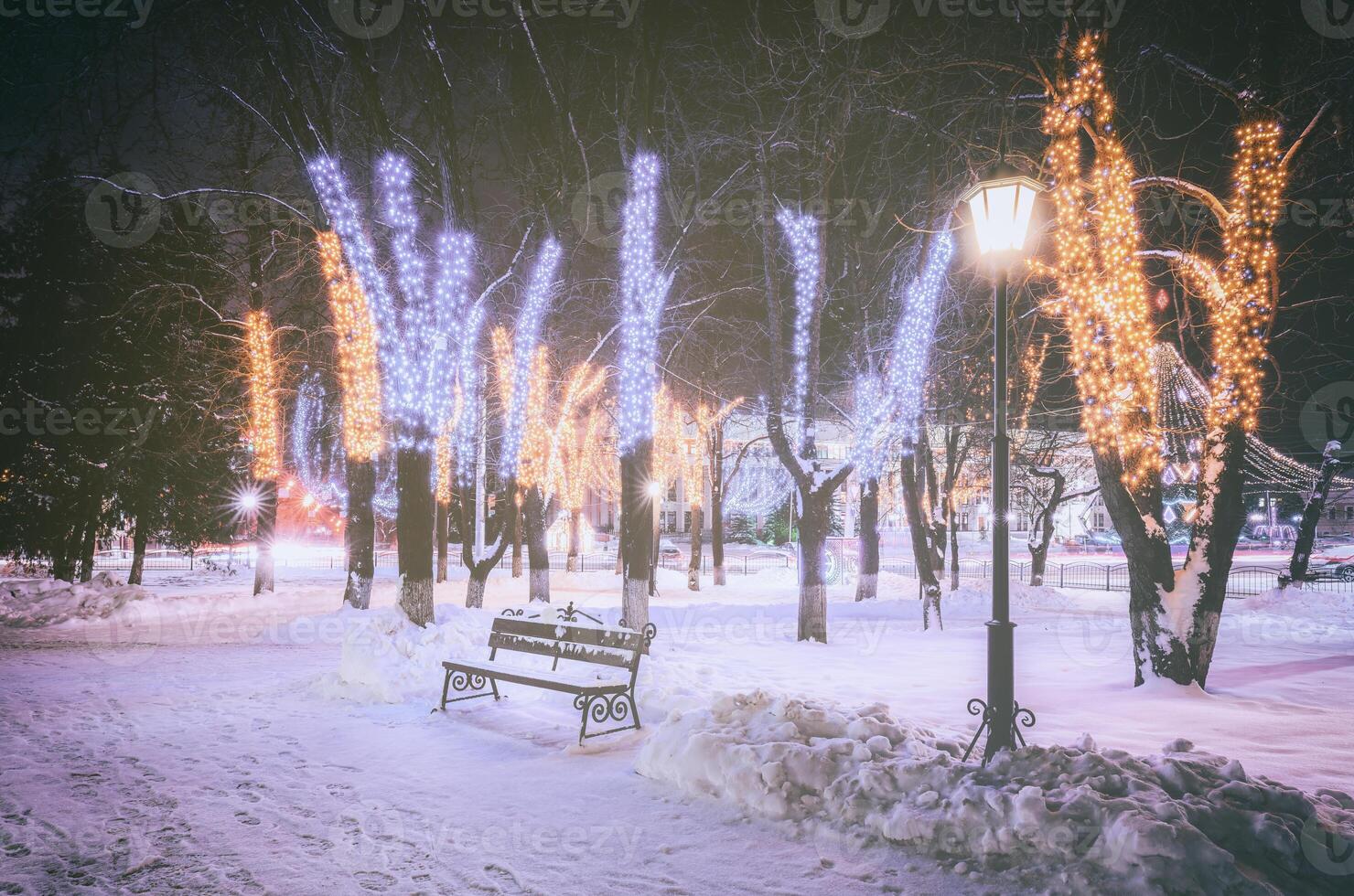 inverno parque às noite com Natal decorações, brilhando lanternas, calçada coberto com neve e árvores vintage filme estética. foto