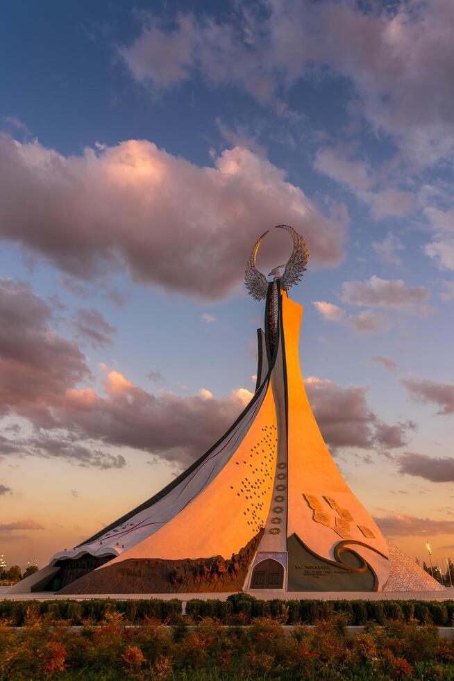 uzbequistão, Tashkent - Outubro 4, 2023 monumento do independência dentro a Formato do uma estela com uma humo pássaro em uma crepúsculo com cliody céu dentro a Novo uzbequistão parque. foto