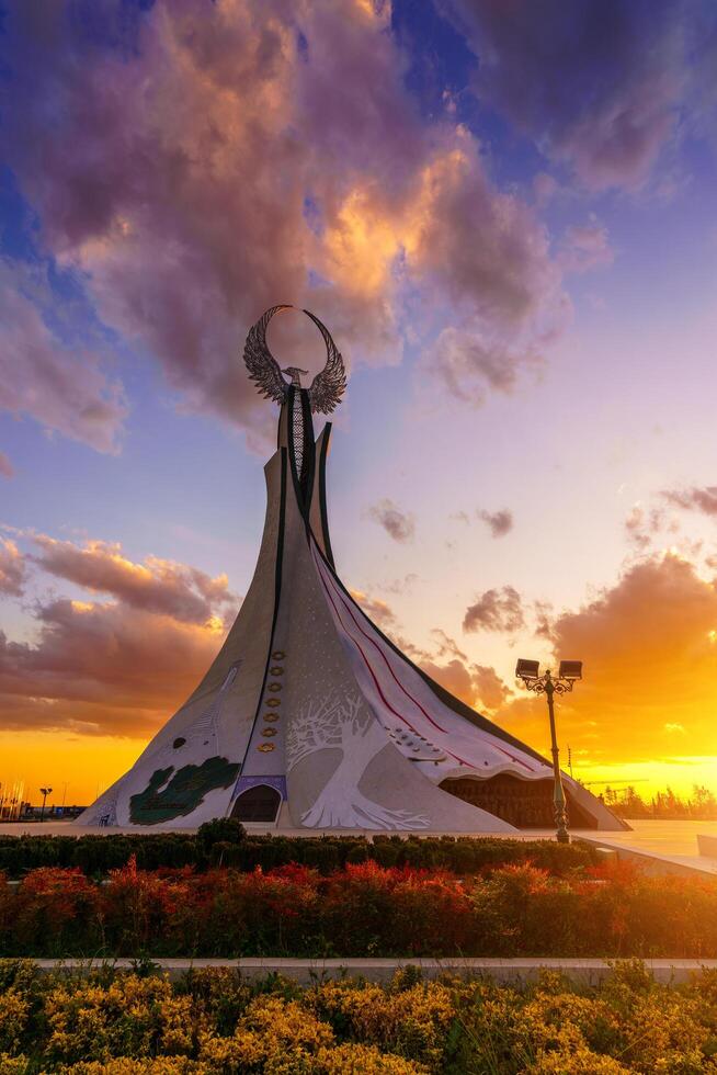 uzbequistão, Tashkent - Outubro 4, 2023 monumento do independência dentro a Formato do uma estela com uma humo pássaro em uma crepúsculo com cliody céu dentro a Novo uzbequistão parque. foto