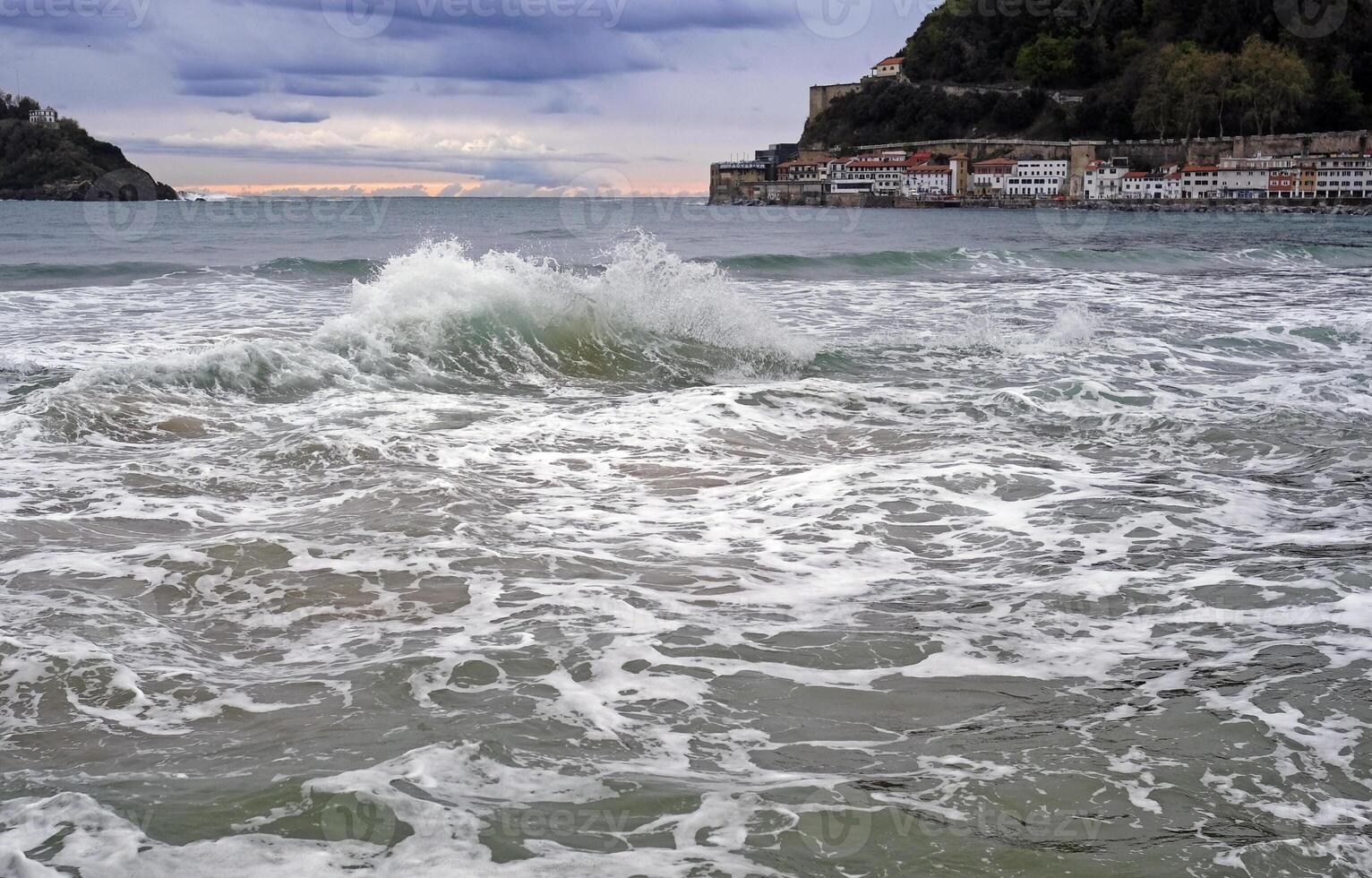 uma onda rompe dentro a baía do san sebastião, Espanha, durante pôr do sol foto