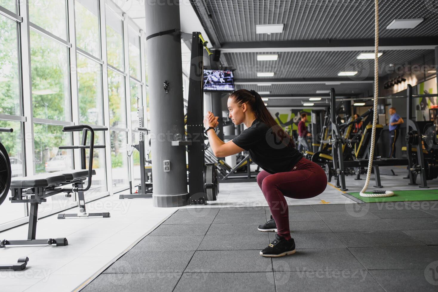 lado Visão retrato do uma jovem mulher fazendo agachamentos às ginástica academia. foto