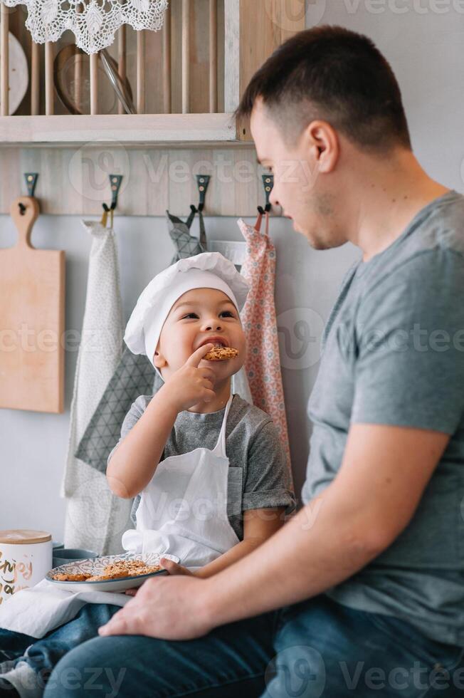 jovem homem e dele filho com forno Folha dentro cozinha. pai com pequeno filho em a cozinha foto