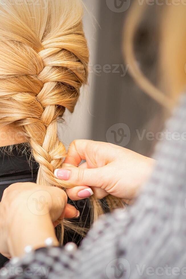 trança trança. mãos do fêmea cabeleireiro tranças grandes trança para uma Loiras mulher dentro uma cabelo salão. foto