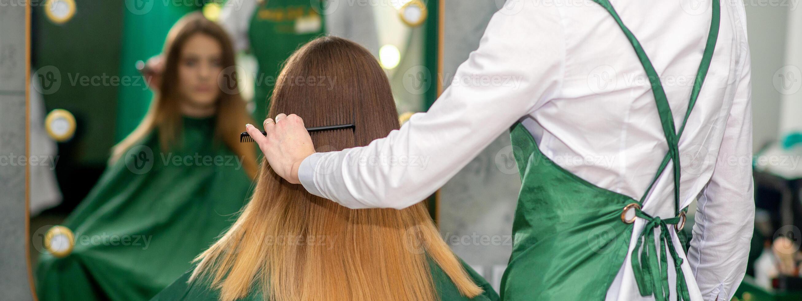 uma fêmea cabeleireiro é pentear a grandes Castanho cabelo do uma jovem mulher às uma salão. foto