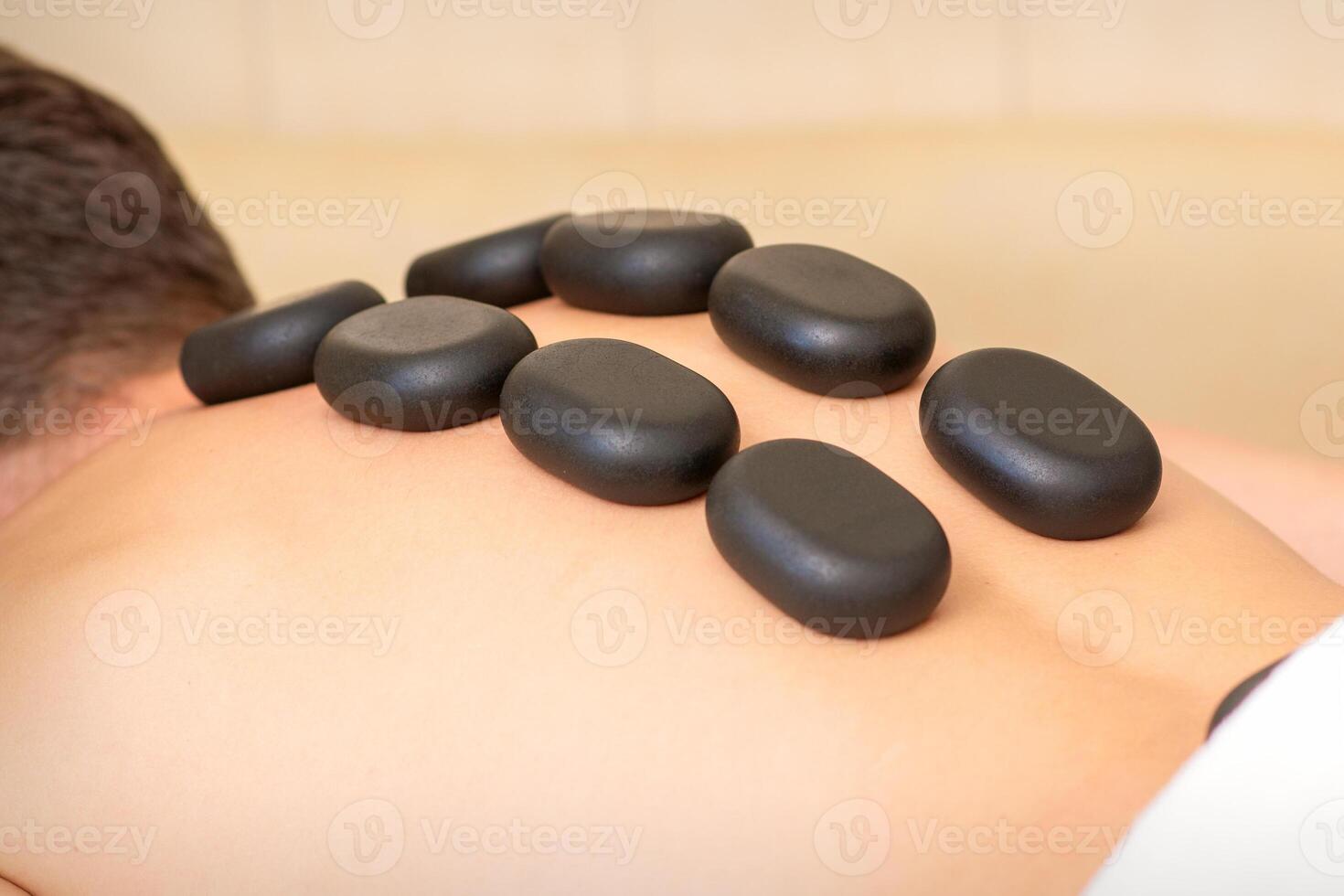 quente pedra massagem terapia. caucasiano jovem homem obtendo uma quente pedra massagem em costas às spa salão. foto