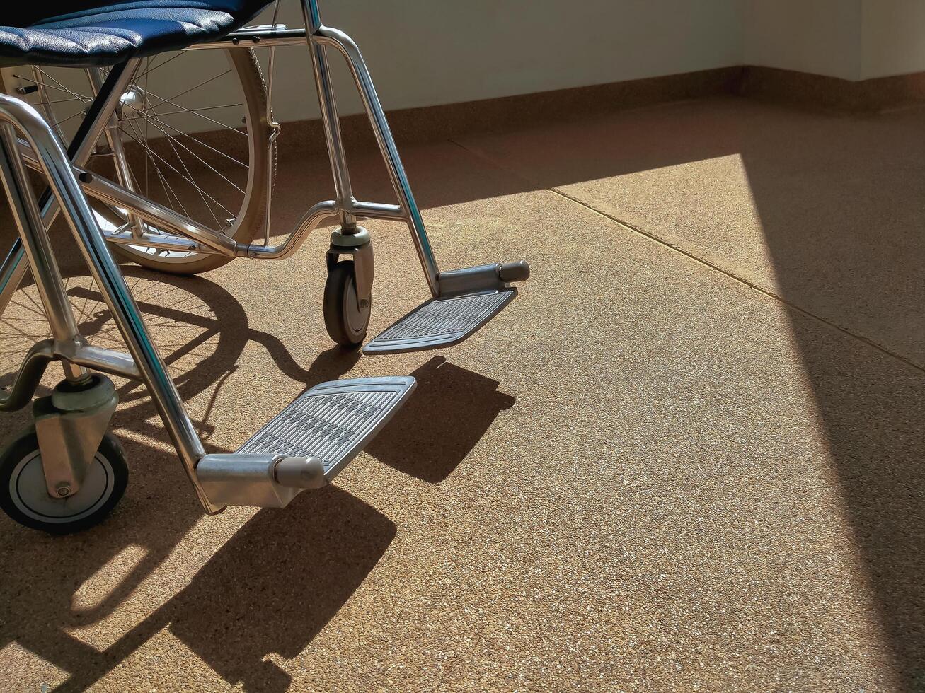 baixo seção do esvaziar cadeira de rodas em calçada com luz solar e sombra em superfície foto
