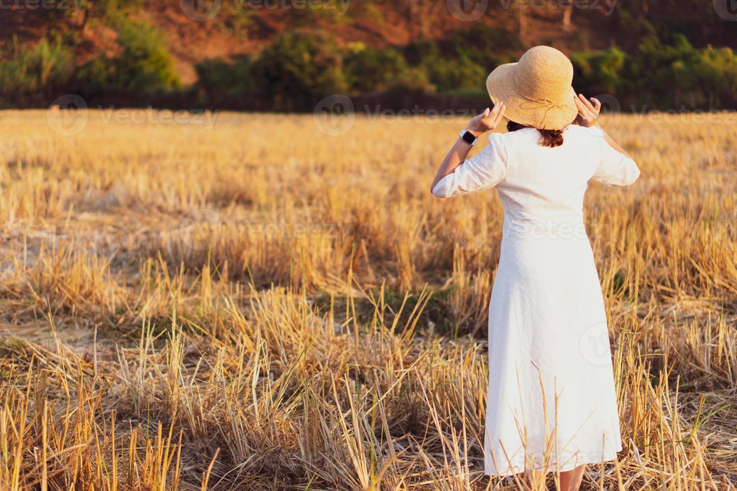 retrato de uma jovem com chapéu de palha e vestido branco em pé no arrozal seco ao pôr do sol foto