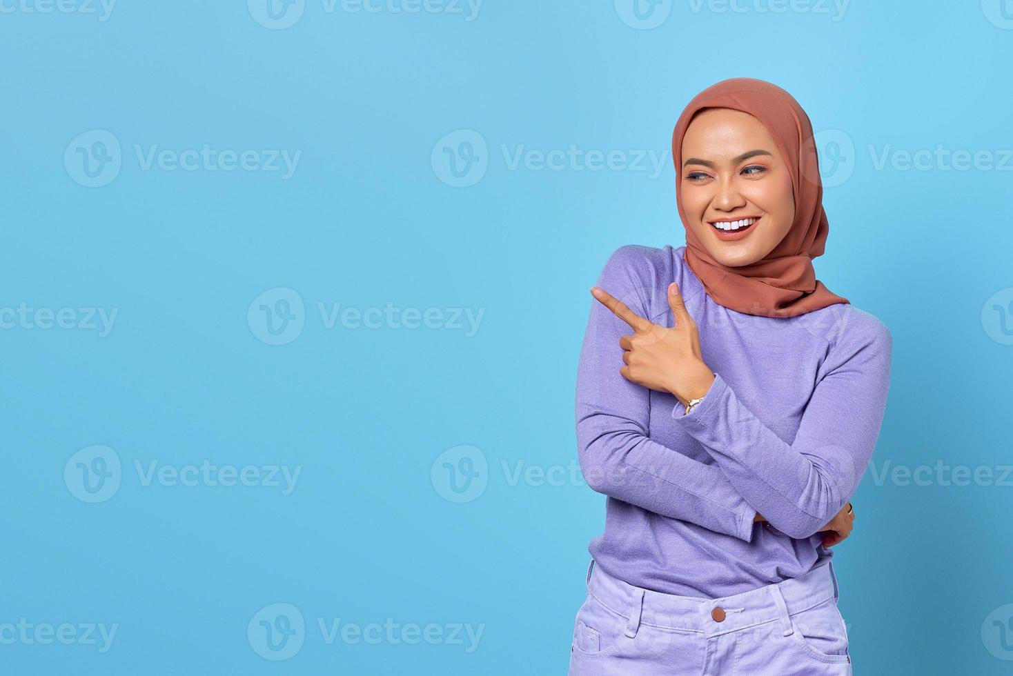 retrato de uma jovem mulher asiática sorridente apontando o dedo para o espaço da cópia sobre fundo azul foto