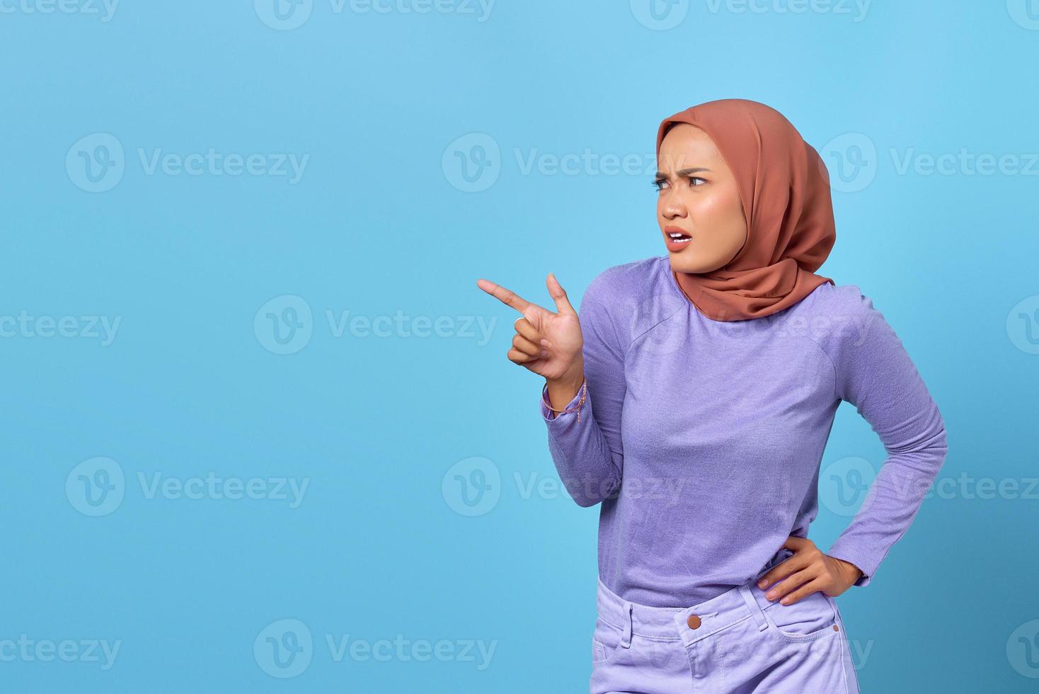 retrato de uma jovem asiática chocada apontando o dedo para o espaço da cópia em fundo azul foto
