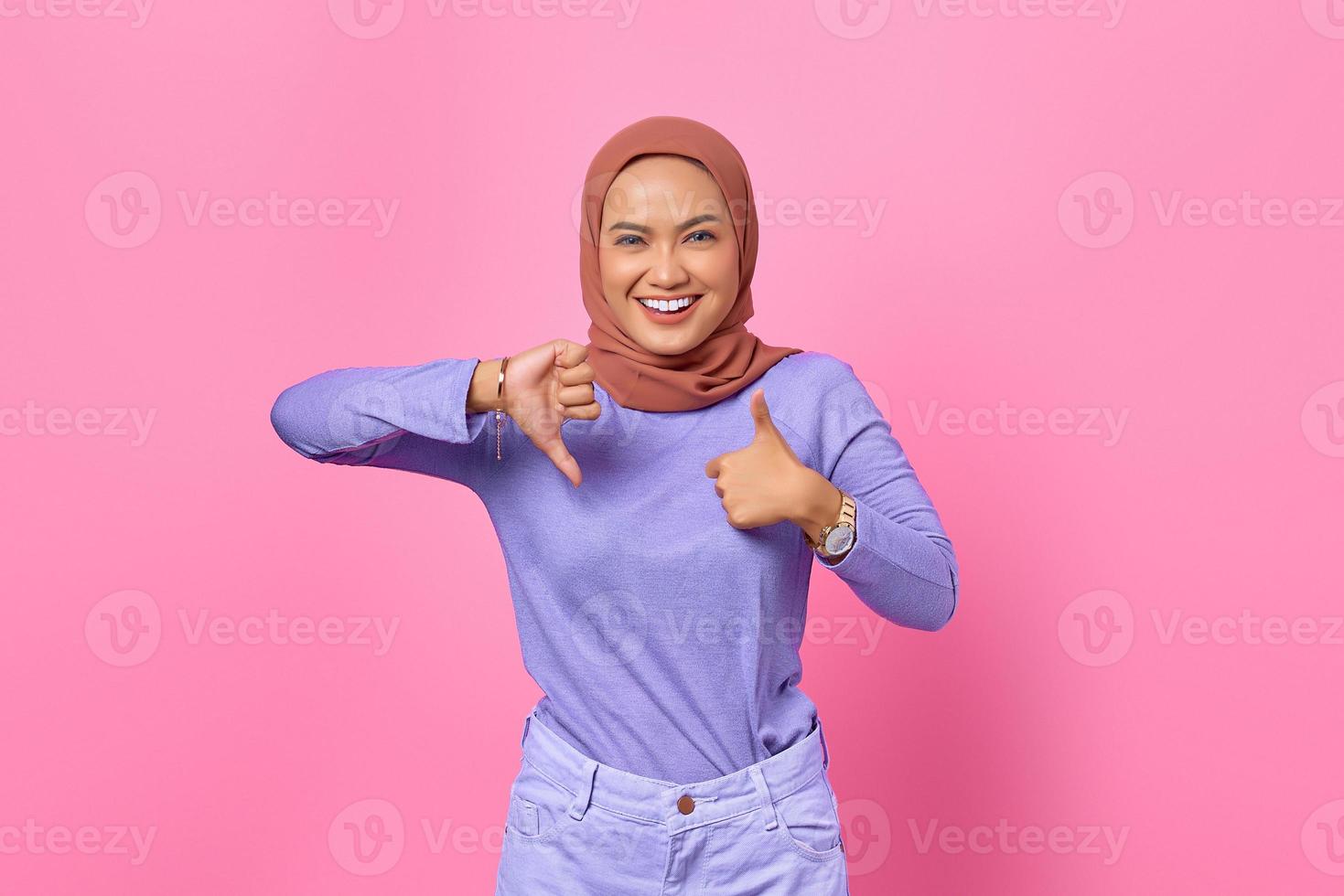 alegre linda jovem asiática mostrando os polegares para cima e para baixo no fundo rosa foto