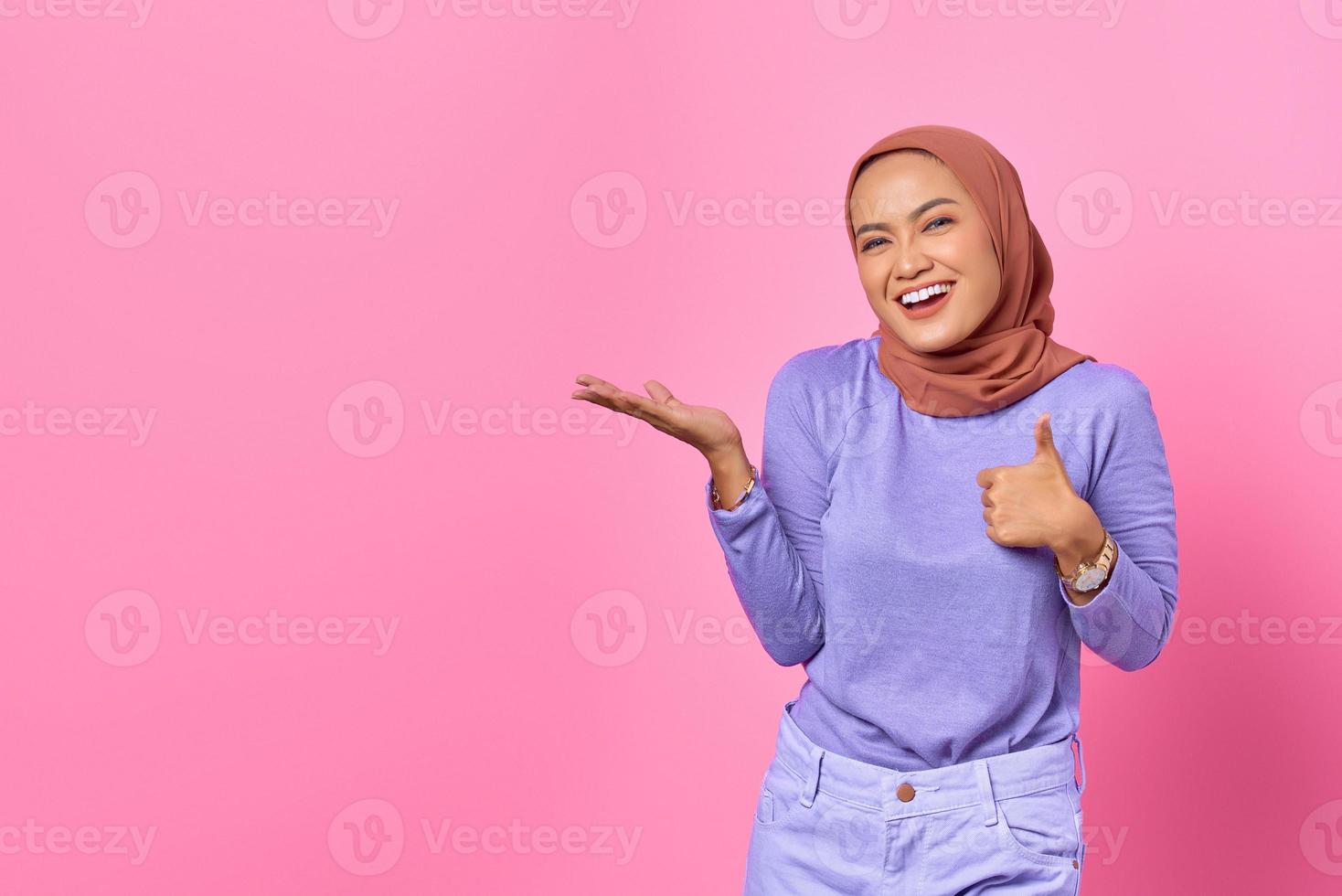 retrato de uma jovem mulher asiática sorridente, mostrando as palmas das mãos e os polegares para cima no fundo rosa foto