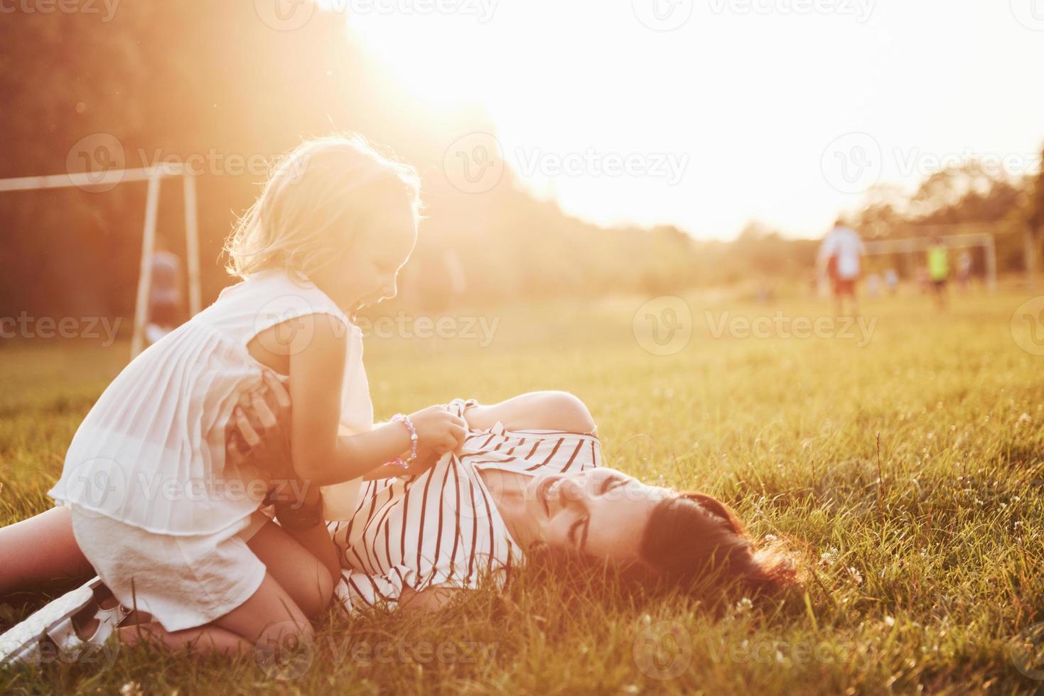 feliz mãe e filha se abraçando em um parque ao sol em um fundo de verão brilhante de ervas. foto