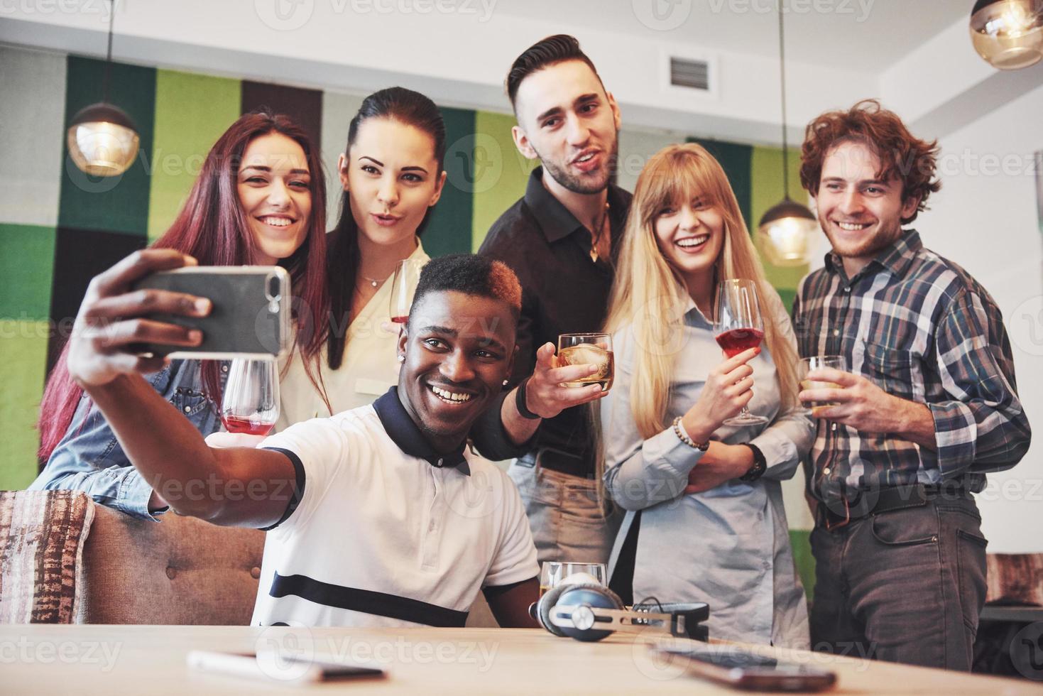 amigos se divertindo no restaurante. três meninos e três meninas fazendo selfie e rindo. no primeiro plano menino segurando o telefone inteligente. todos usam roupas casuais foto