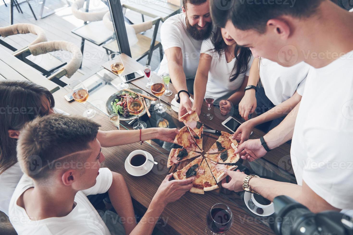 pizza saborosa na mesa, com um grupo de jovens sorridentes descansando no bar foto