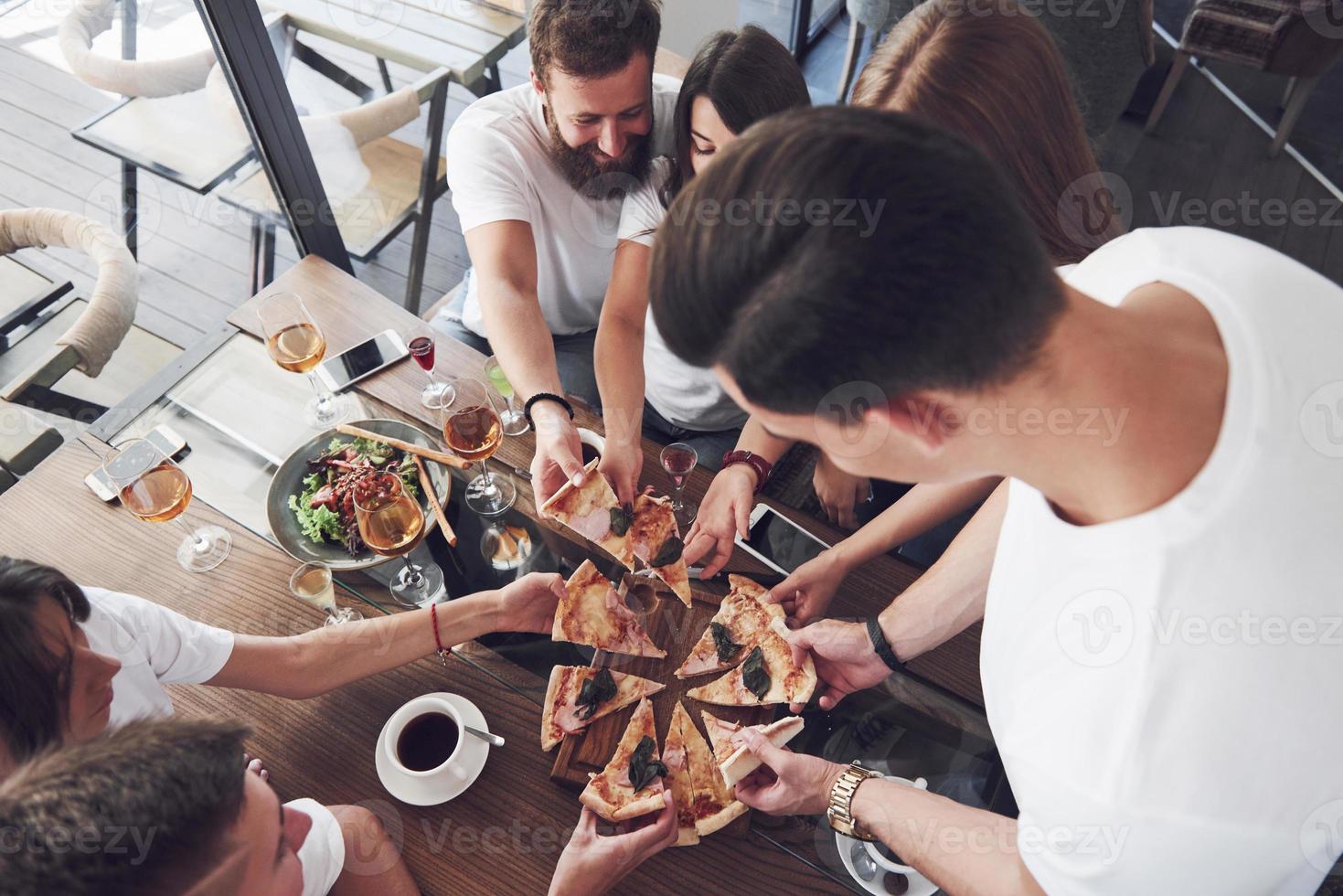 pizza saborosa na mesa, com um grupo de jovens sorridentes descansando no bar foto