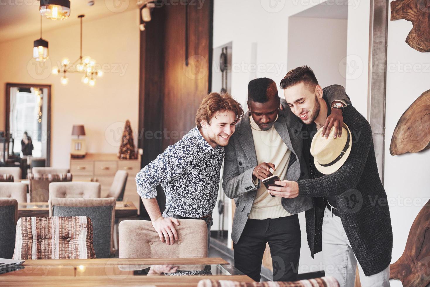 velhos amigos alegres se comunicam uns com os outros e assistem ao telefone no bar. conceito de entretenimento e estilo de vida. pessoas conectadas por wi-fi em reunião de mesa de bar foto