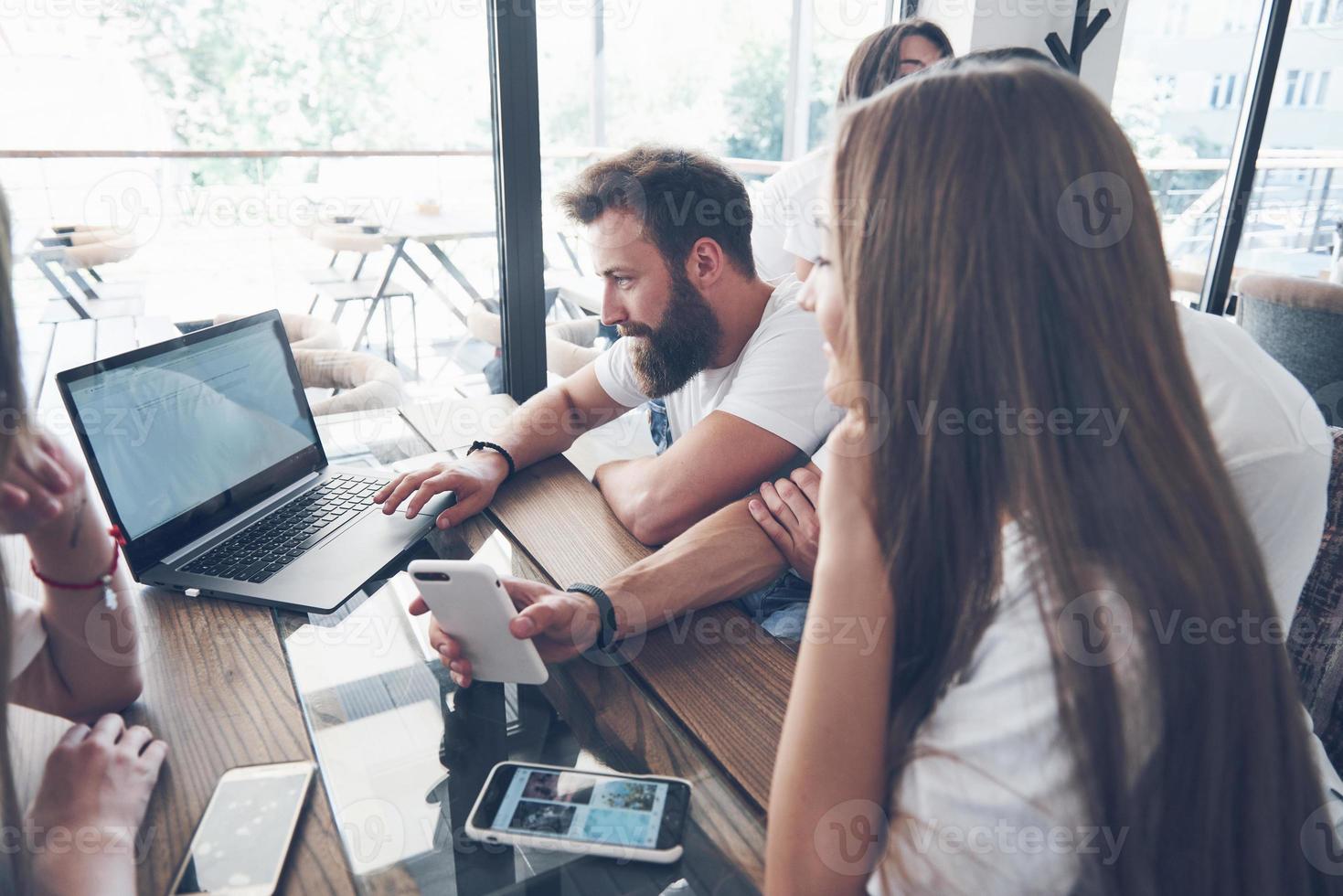 um grupo de jovens com gadgets e um laptop organizam um brainstorm e se comunicam entre si. o conceito de desenvolver um jovem negócio foto