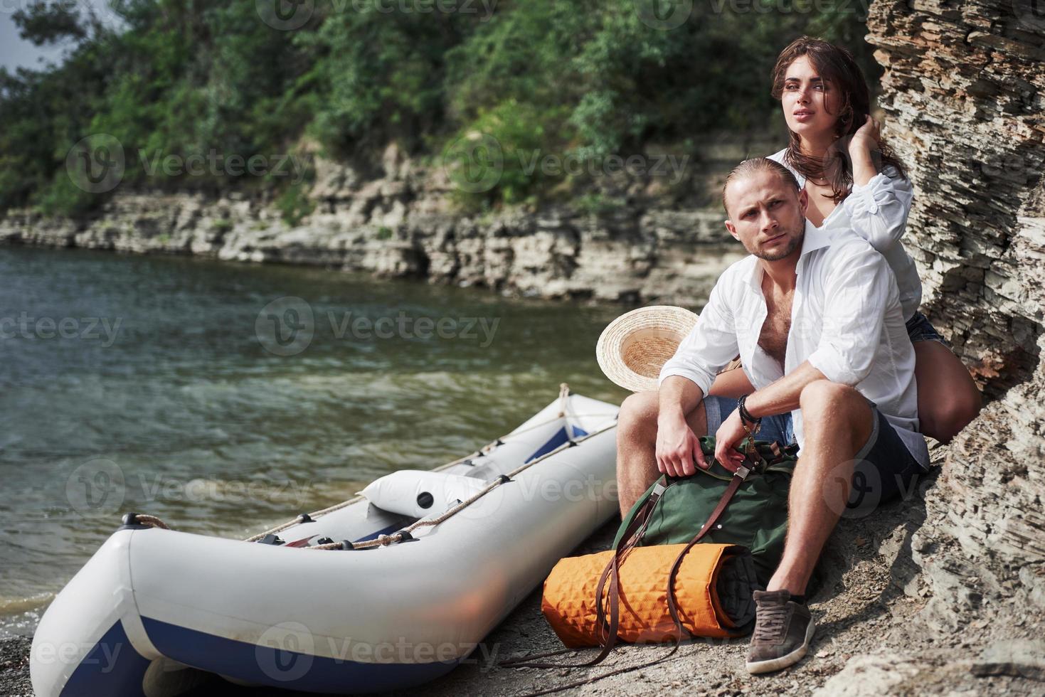 jovem bonito e casal no fundo do rio. um cara e uma garota com mochilas estão viajando de barco. conceito de verão do viajante foto