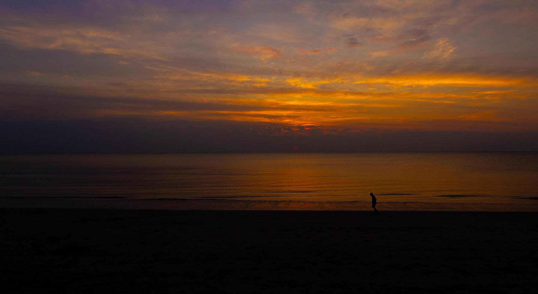 silhuetas uma sereno pôr do sol sobre a praia, a céu do laranja e fundição foto