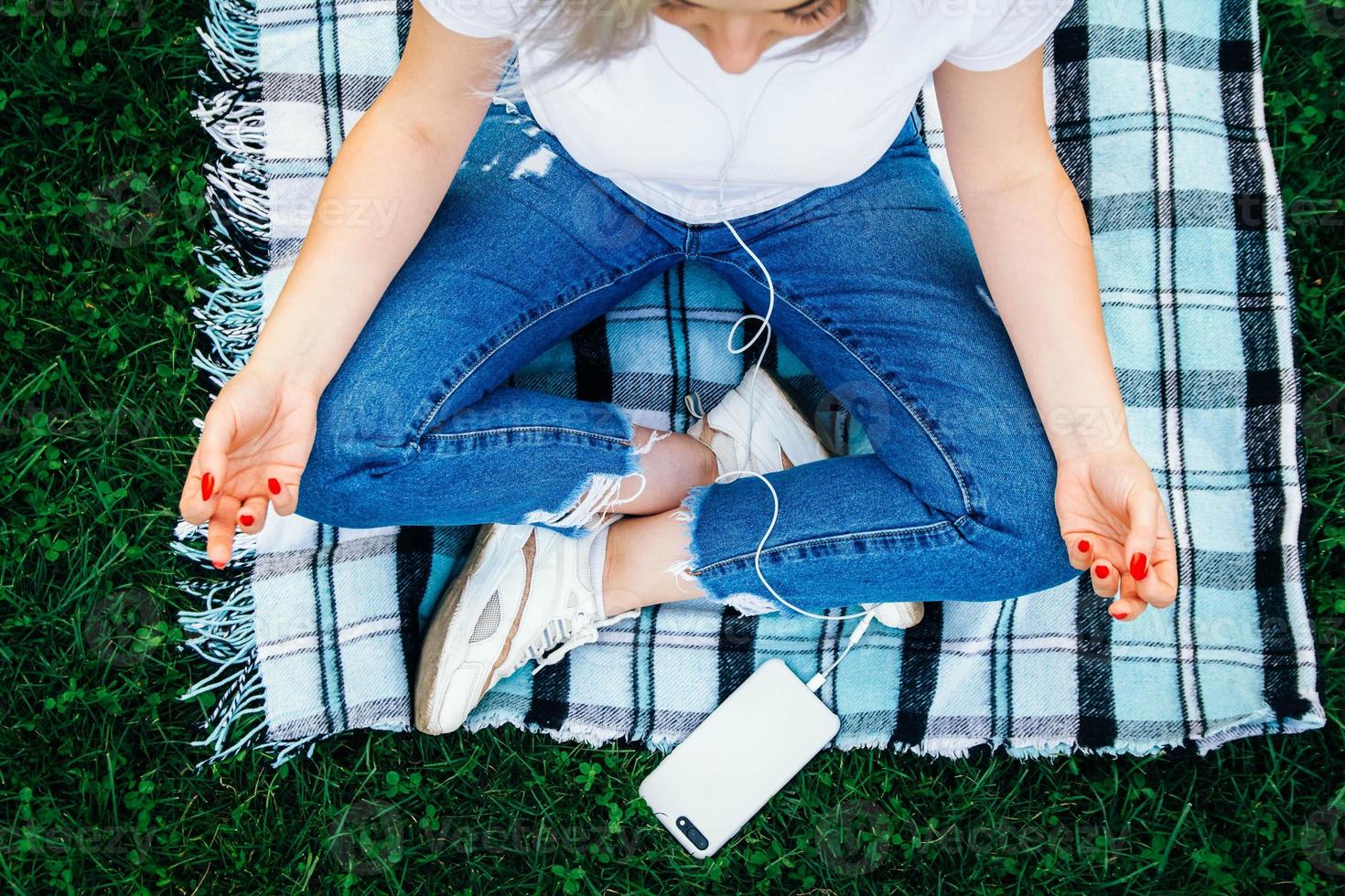 mulher com fones de ouvido sentada em pose meditativa na grama verde foto