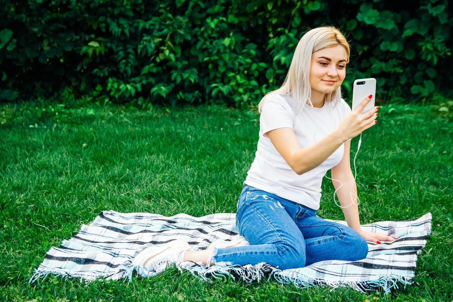 mulher com fones de ouvido e smartphone na grama verde foto