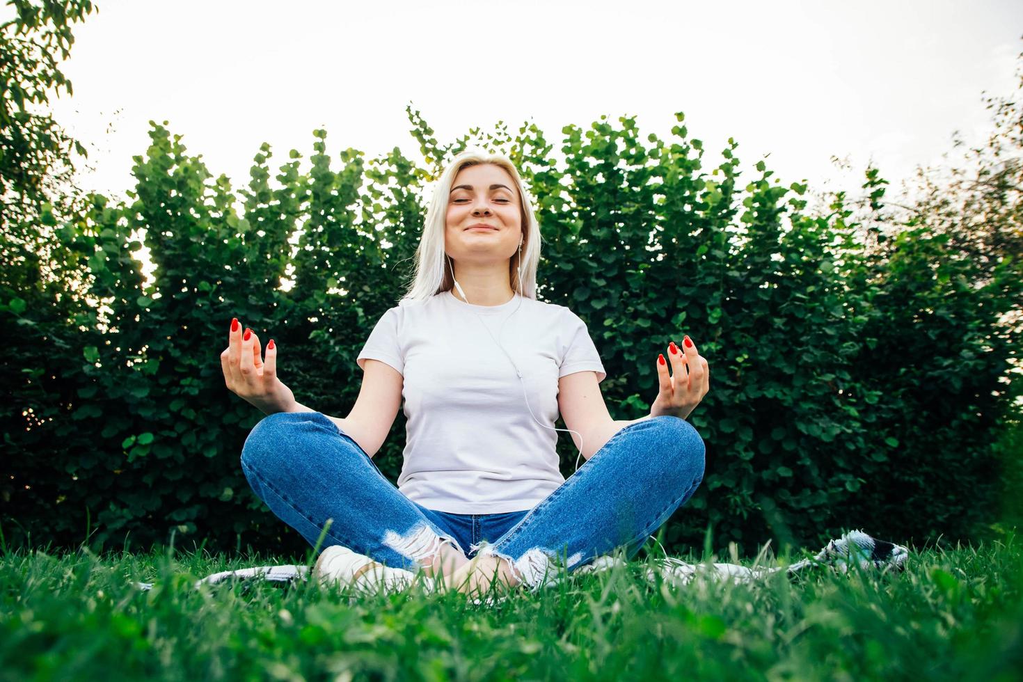 mulher com fones de ouvido sentada em pose meditativa na grama verde foto