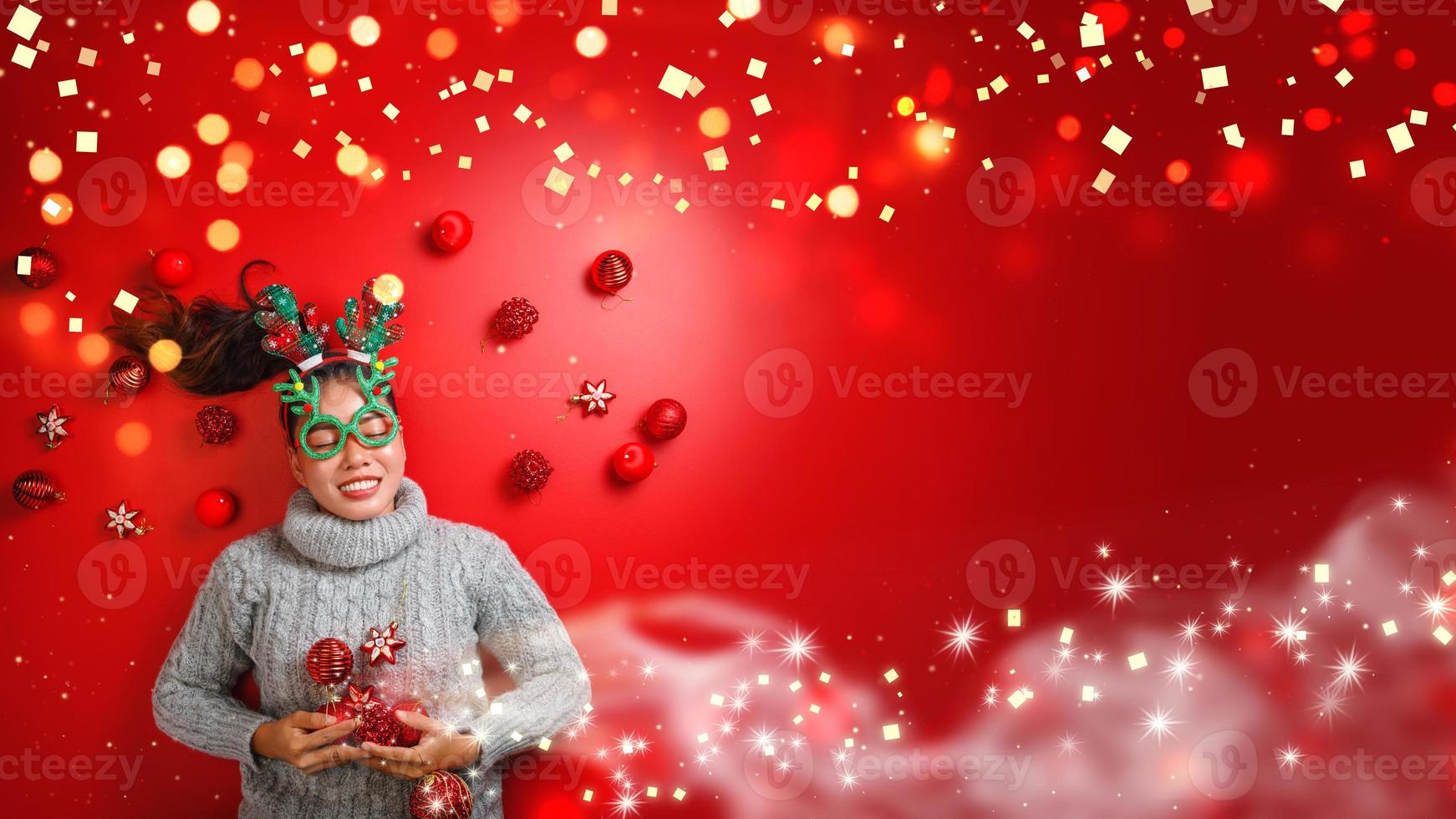 Natal ano novo. jovem vestida com uma camisola quente com adereços bola vermelha com enfeites de Natal em férias em fundo vermelho brilho. conceito, feliz Natal. foto