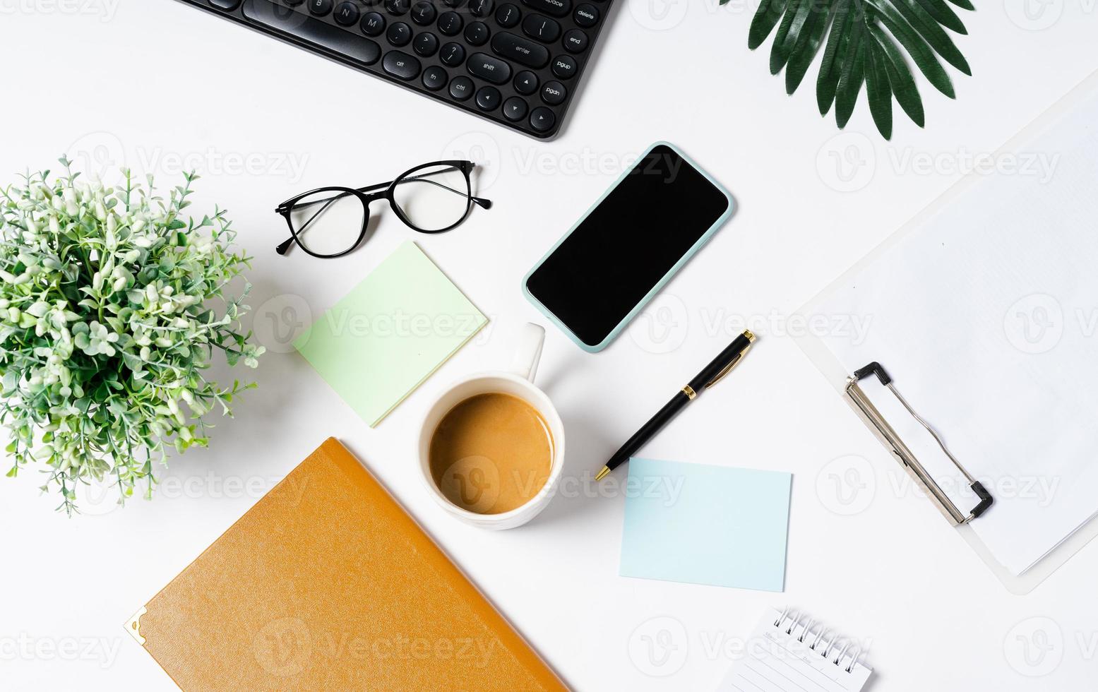 vista superior do café, livro, caderno, caneta, teclado, telefone em fundo branco foto