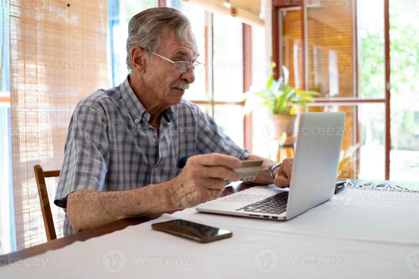 retrato de homem mais velho pagando online com cartão de crédito em casa foto