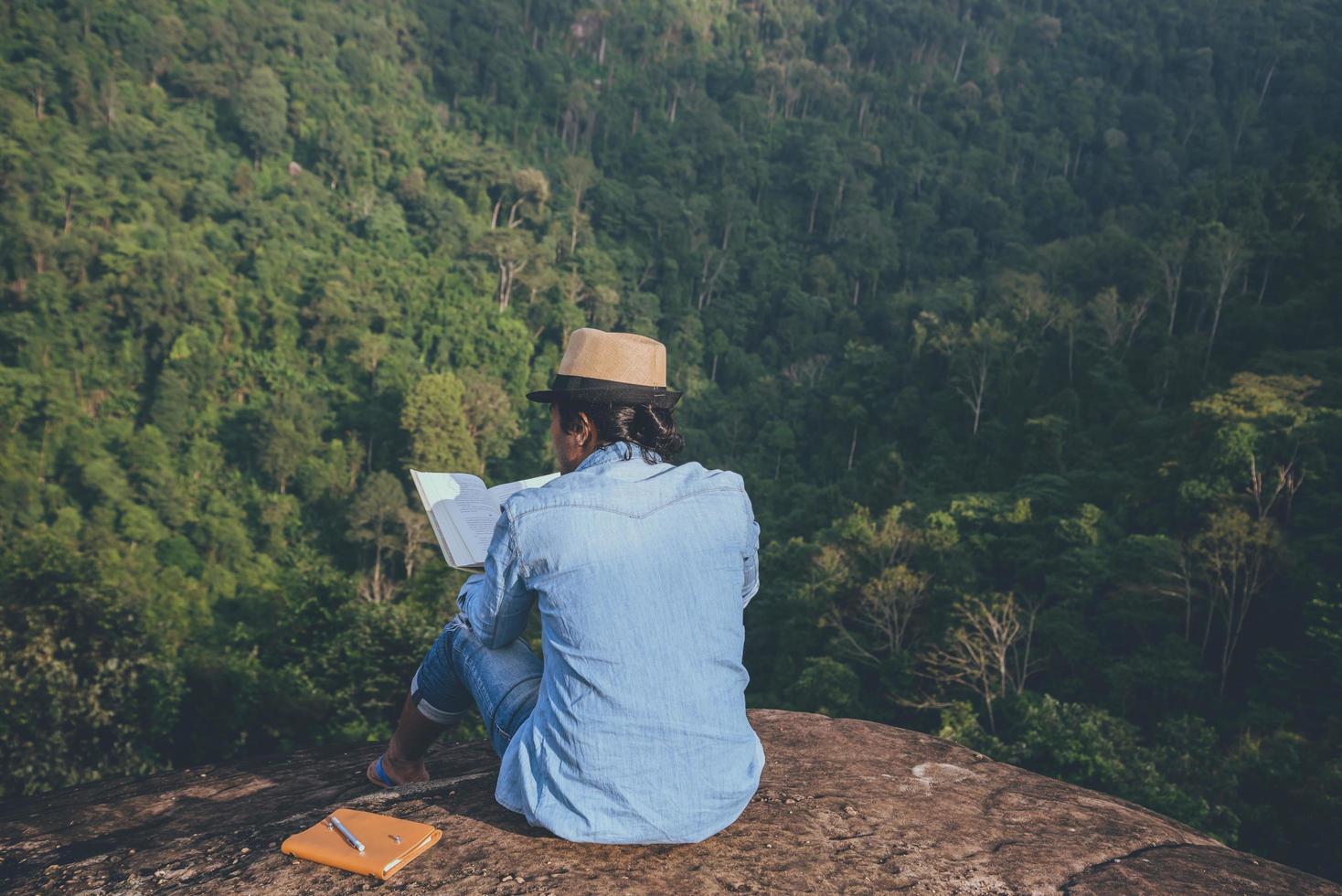 homem asiático viajar relaxar no feriado. assentos relaxem, leiam livros em penhascos rochosos. na montanha. Na Tailândia foto