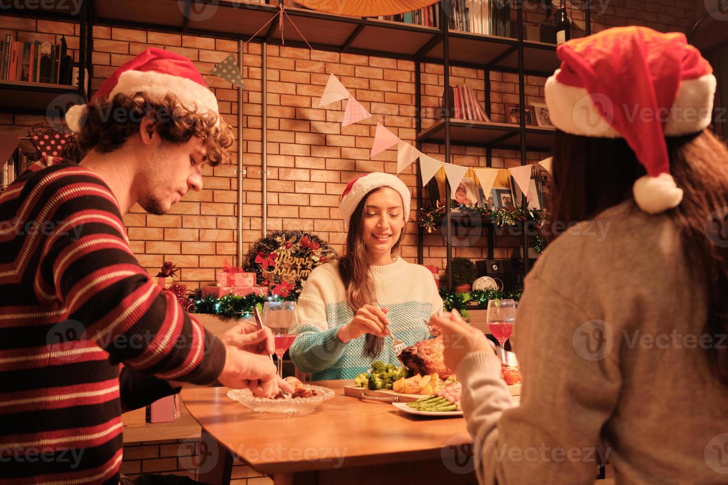 os amigos se divertem comendo o jantar à mesa com comidas especiais, como peru assado e vinho na sala de jantar de sua casa, decorada com enfeites, festival de natal e festa de celebração de ano novo. foto