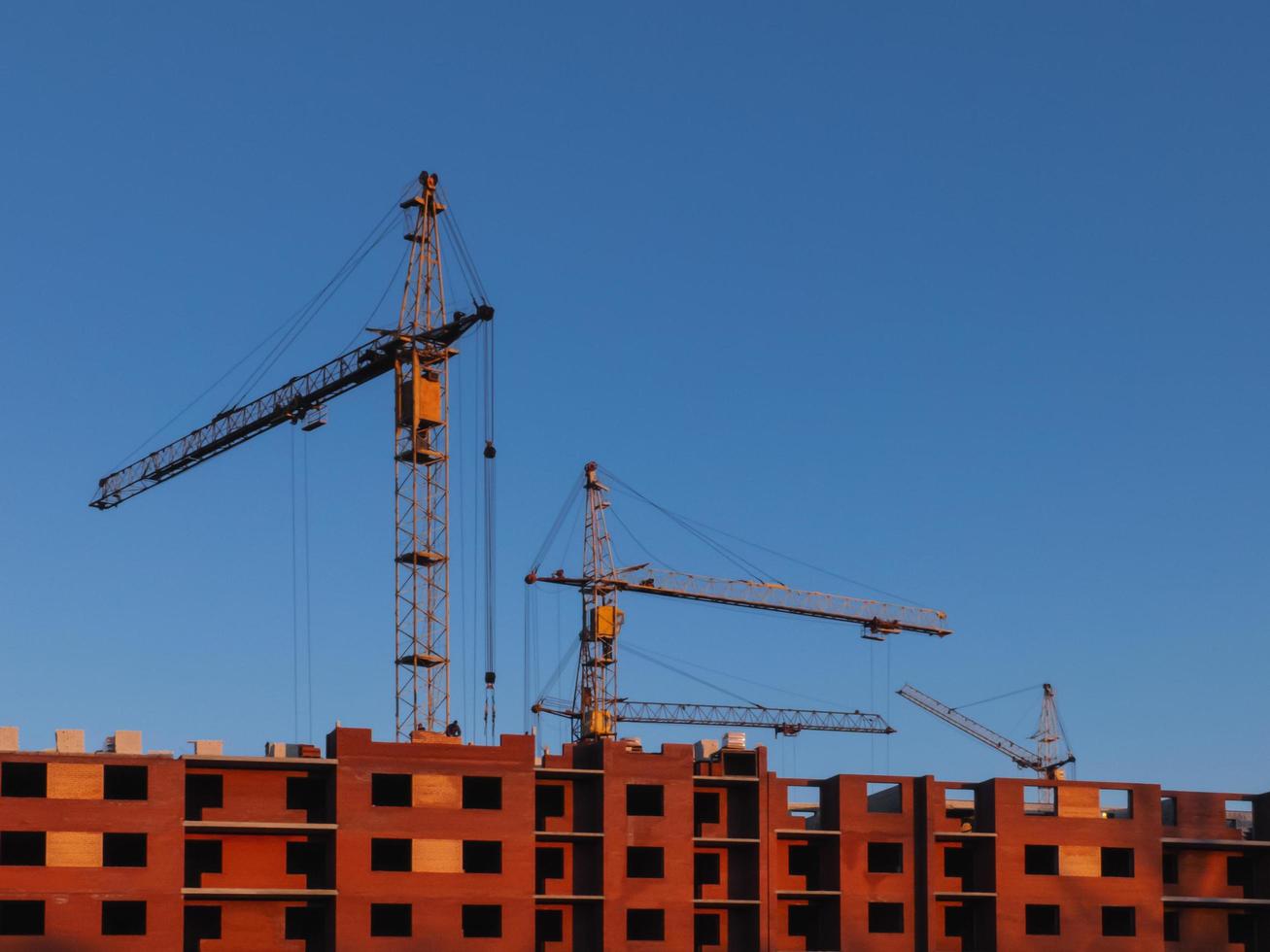 guindastes de construção amarelos trabalhando na construção de um edifício de vários andares de tijolo vermelho. foto