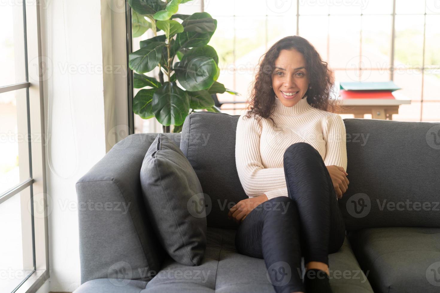 mulher latina sorrindo e sentada no sofá foto