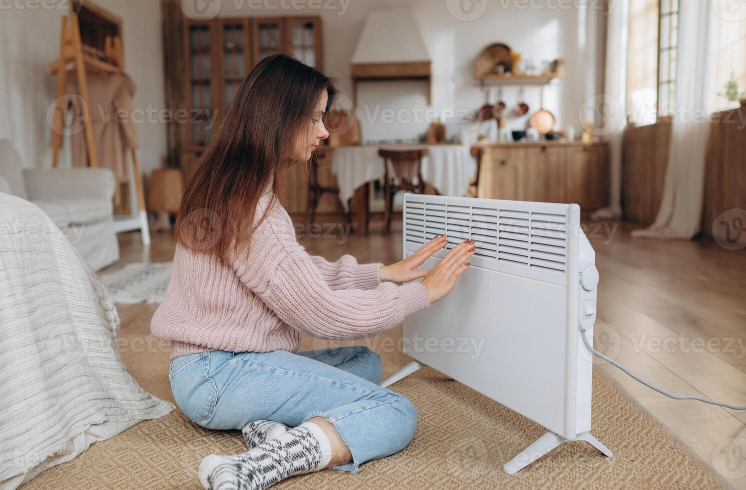 mulher aquecimento mãos perto elétrico aquecedor às lar. usando aquecedor às casa dentro inverno. mulher aquecimento dela mãos. aquecimento temporada. foto