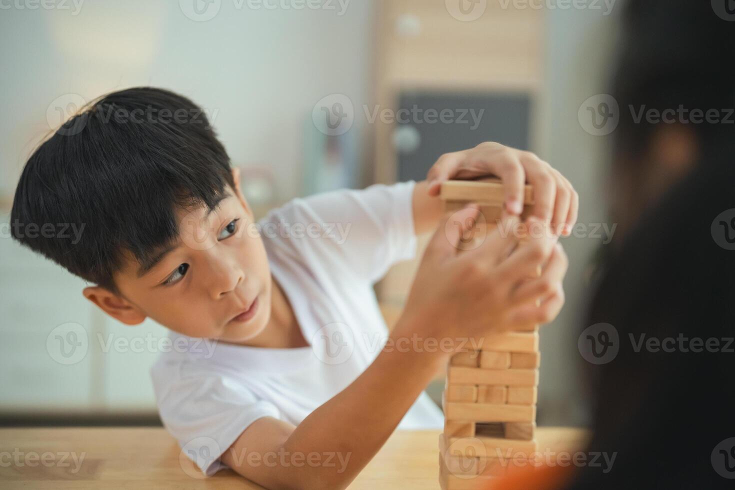 uma jovem Garoto é jogando com uma de madeira quadra torre. ele é focado em a torre e ele é desfrutando ele mesmo foto