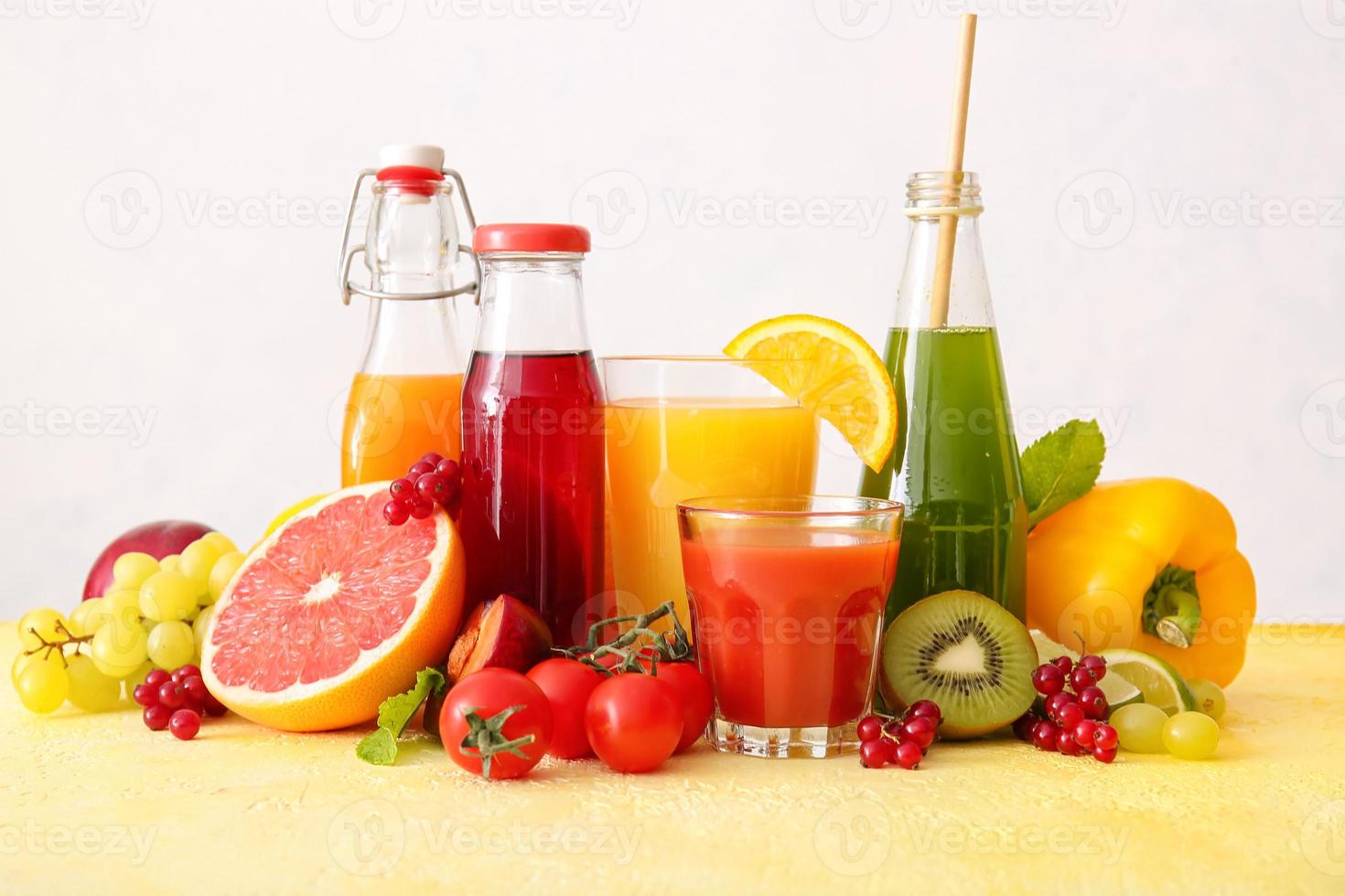 garrafas com sucos saudáveis, frutas e vegetais em fundo claro foto