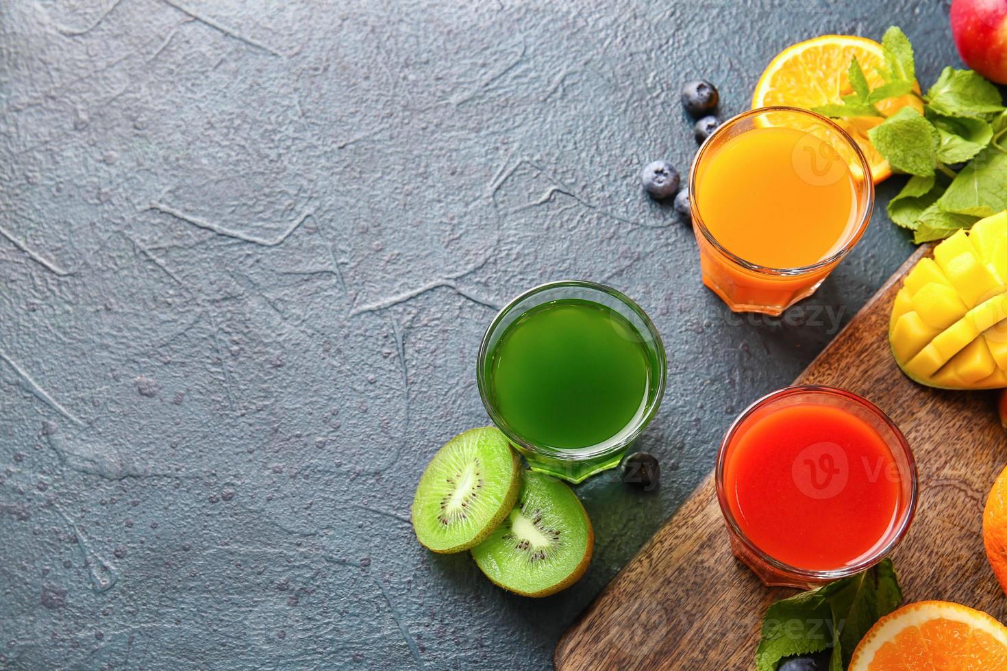 copos com sucos saudáveis, frutas e vegetais em fundo escuro foto