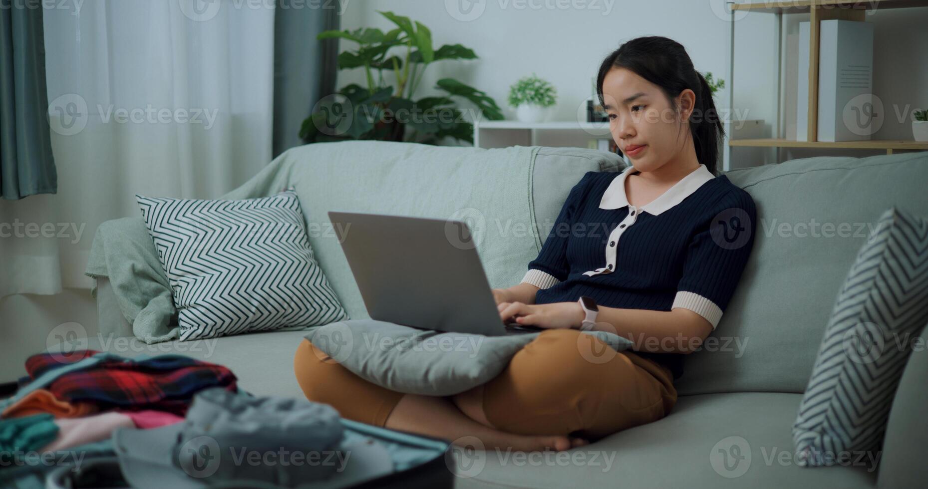 retrato do ásia adolescente mulher sentado em sofá usando computador portátil para preparar reserva hotel e avião bilhete para viagem. mochileiro viagem conceito. foto