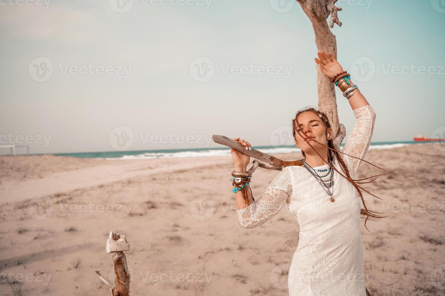 modelo dentro boho estilo dentro uma branco grandes vestir e prata joalheria em a de praia. dela cabelo é trançado, e lá estão muitos pulseiras em dela braços. foto