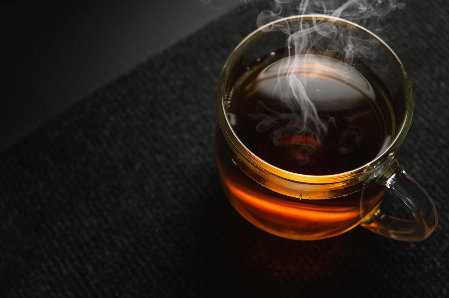 chá preto quente em uma xícara transparente em um fundo preto foto