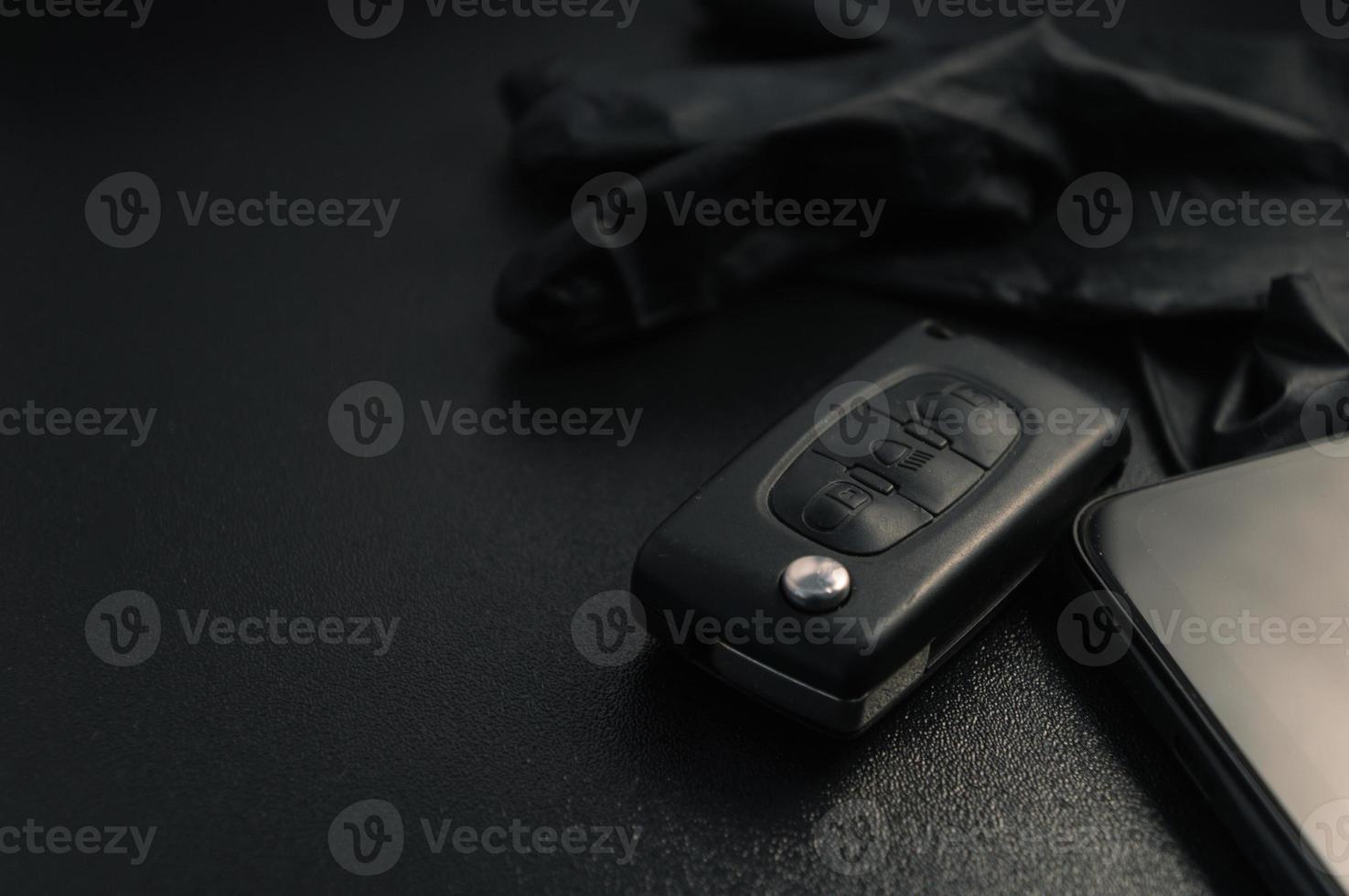 a chave do carro com luvas pretas e um smartphone repousa sobre uma mesa preta foto
