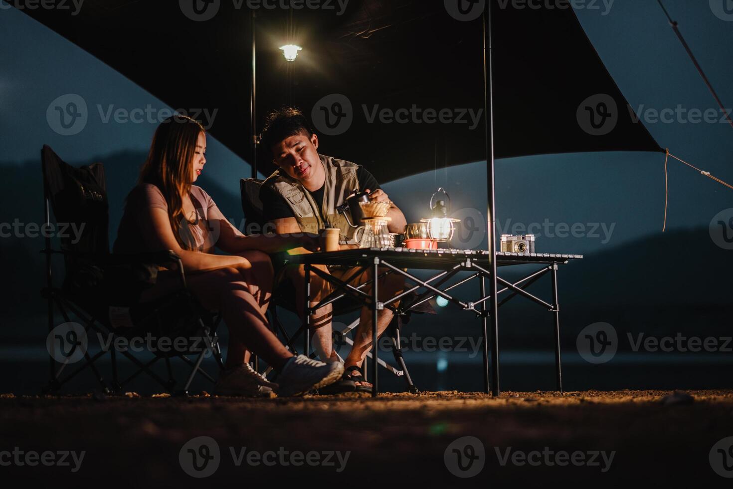 debaixo a noite céu, uma jovem casal ações uma momento sobre bebidas às seus iluminado acampamento, exalando uma acolhedor ambiente. foto
