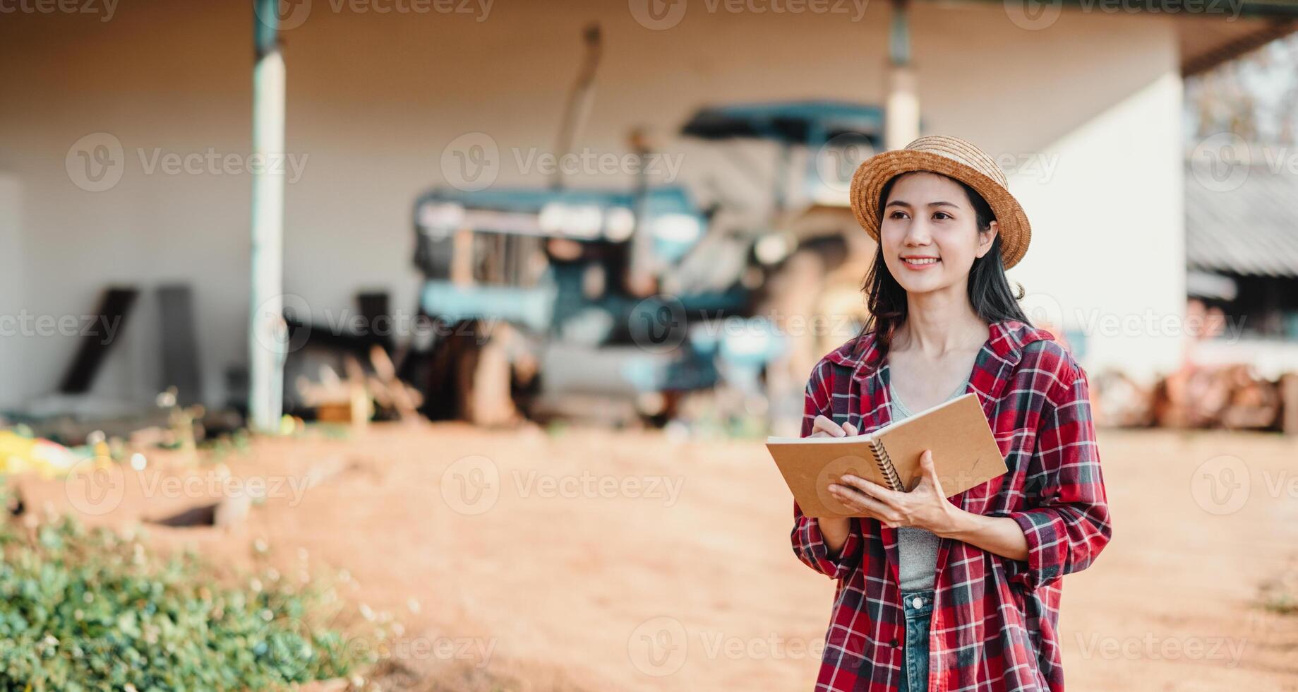 otimista jovem agricultor segurando uma bloco de anotações carrinhos dentro frente do Fazenda equipamento, pronto para enfrentar a dias tarefas. foto