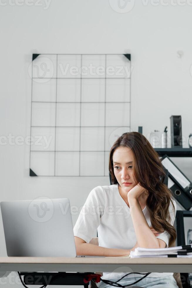 uma mulher é sentado às uma escrivaninha com uma computador portátil e uma pilha do papéis foto