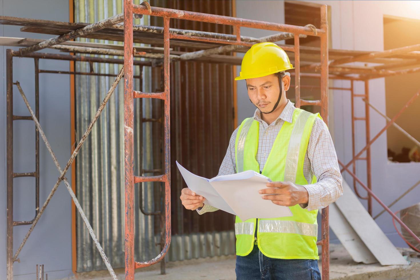 um engenheiro examina a planta baixa do canteiro de obras. foto