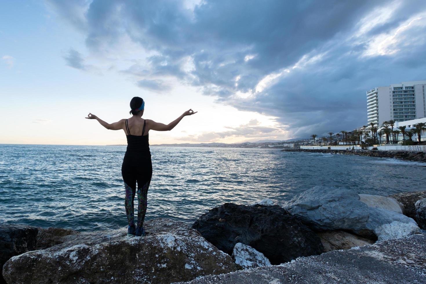mulher praticando ioga de frente para o mar em um dia nublado foto